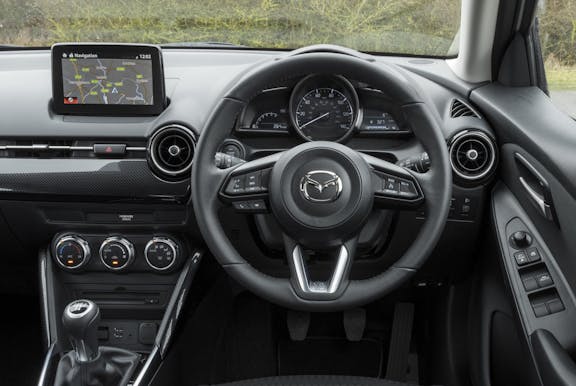 The interior of a Mazda 2 with steering wheel and dashboard in shot