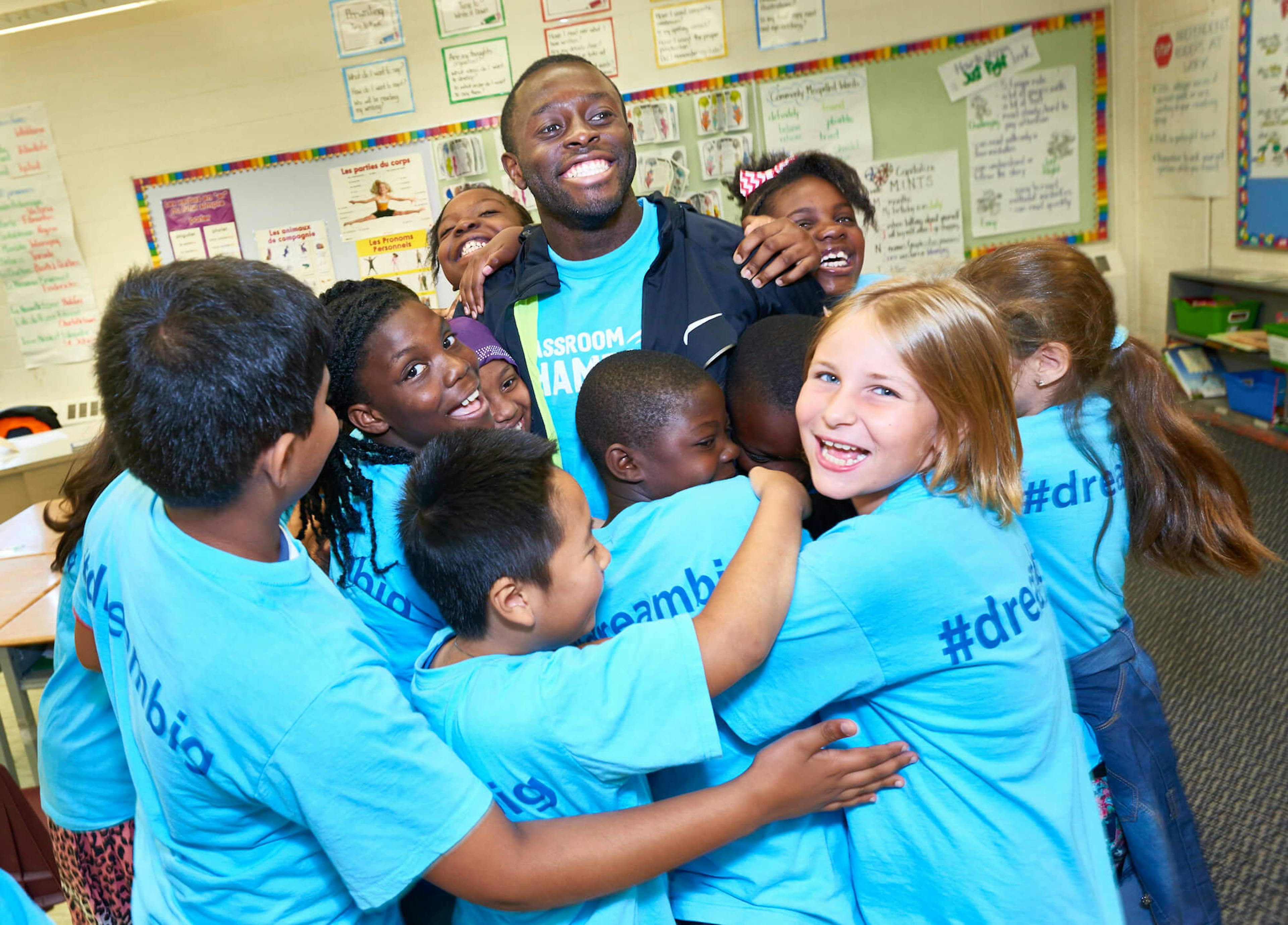 A group of children in Classroom Champions shirts hug an athlete