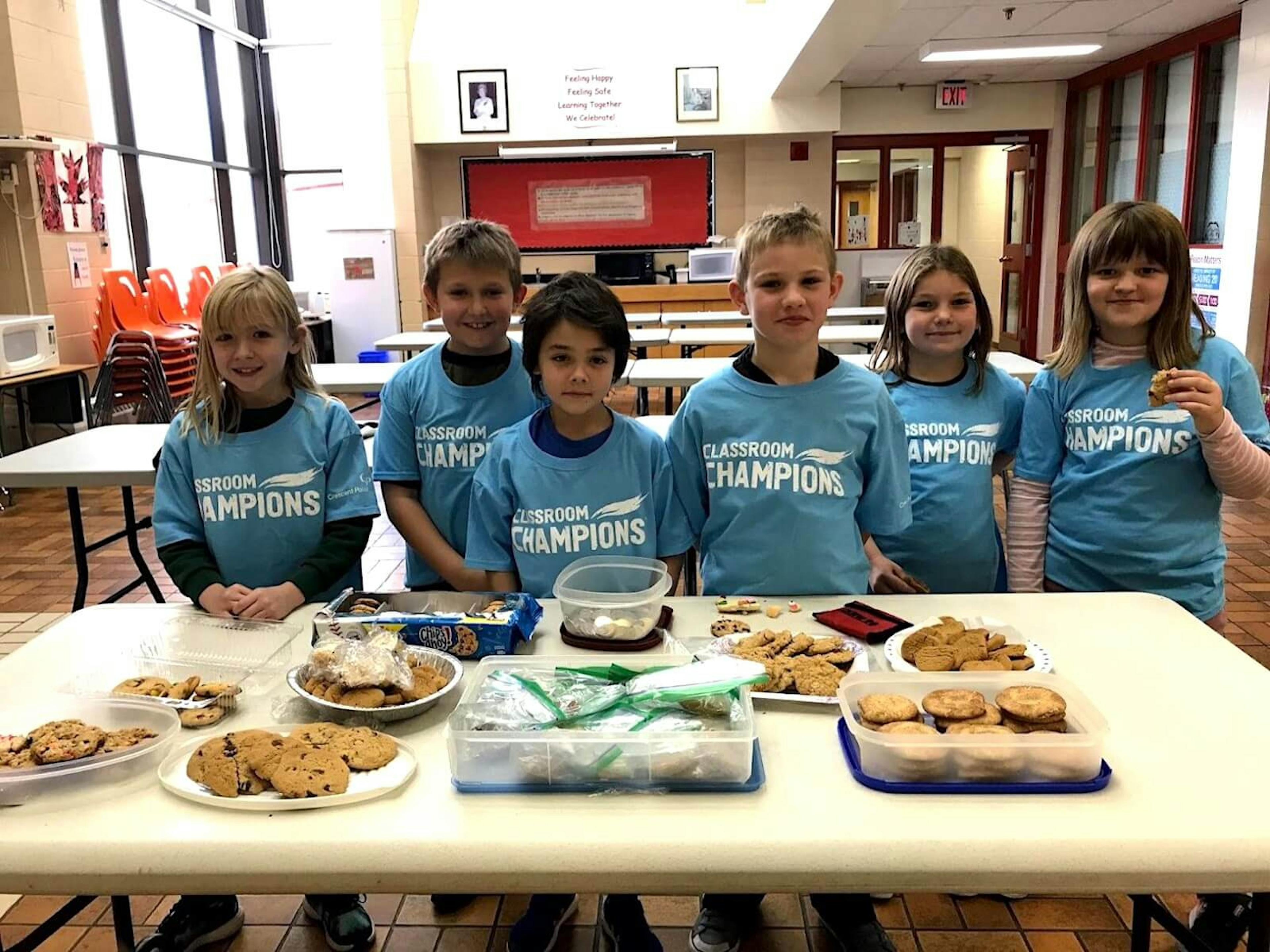Six kids stand in front of a table covered in cookies