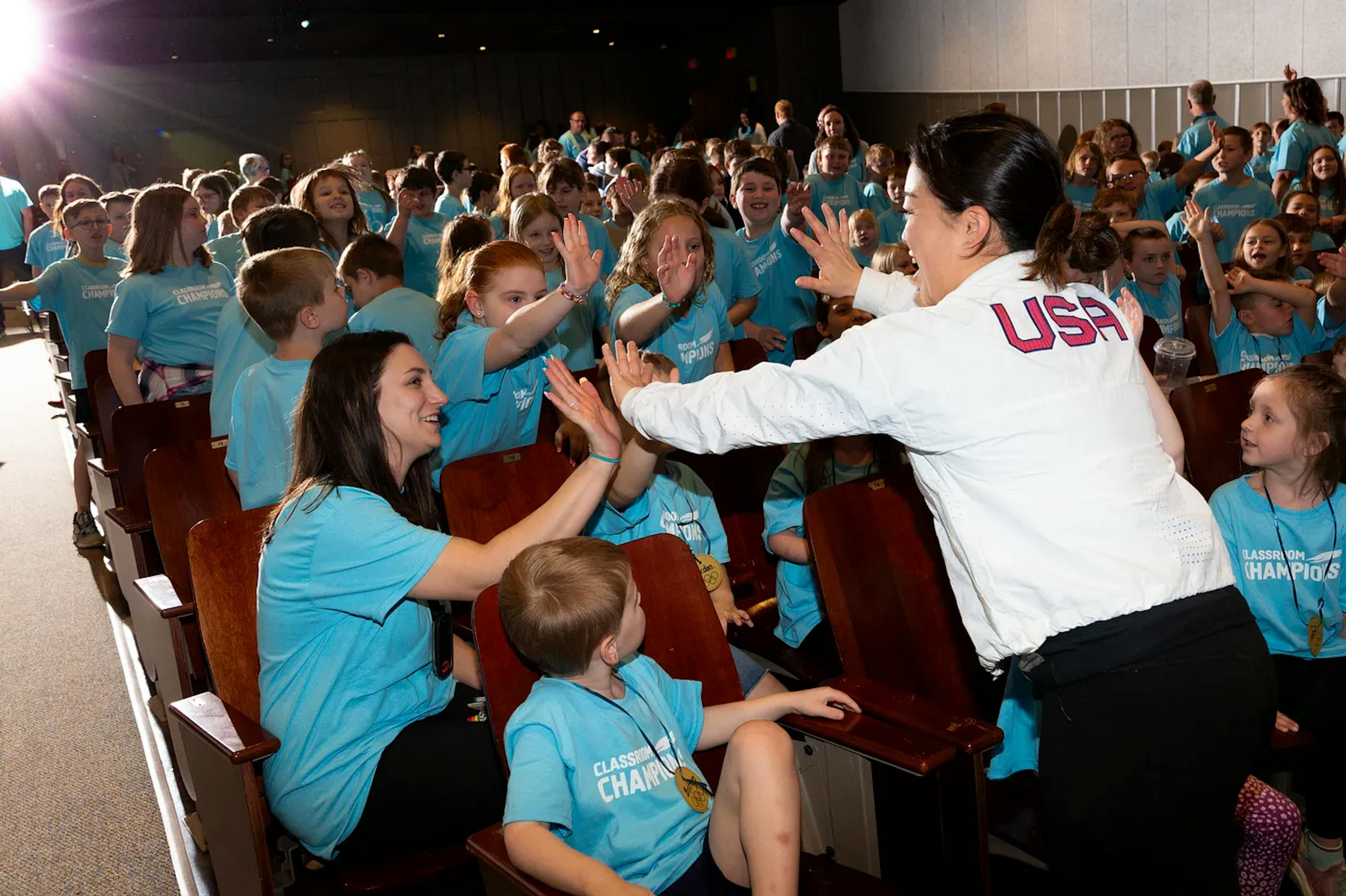 A group of students high-five an athlete in an auditorium