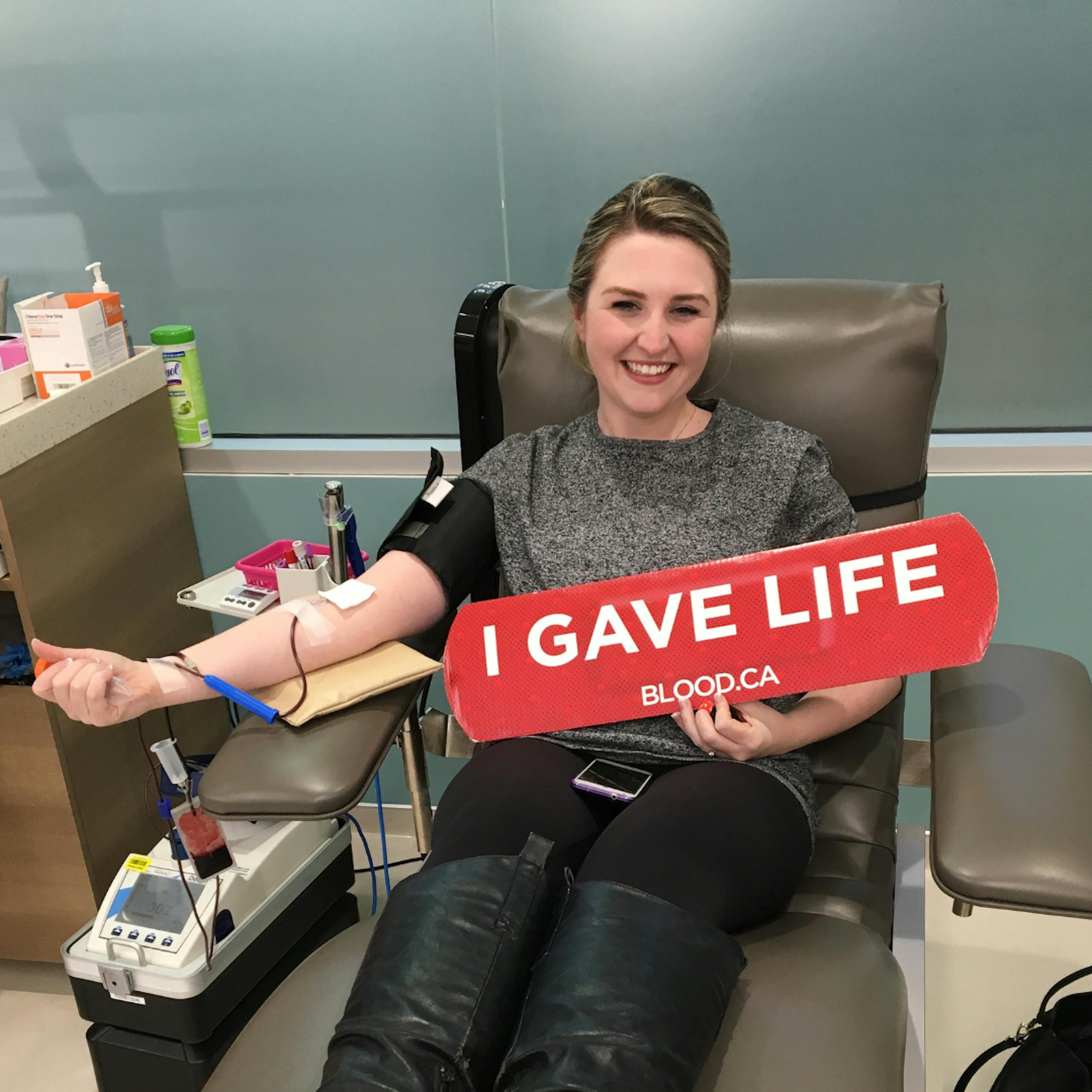 woman donating blood and holding a sign that reads 'I gave life'