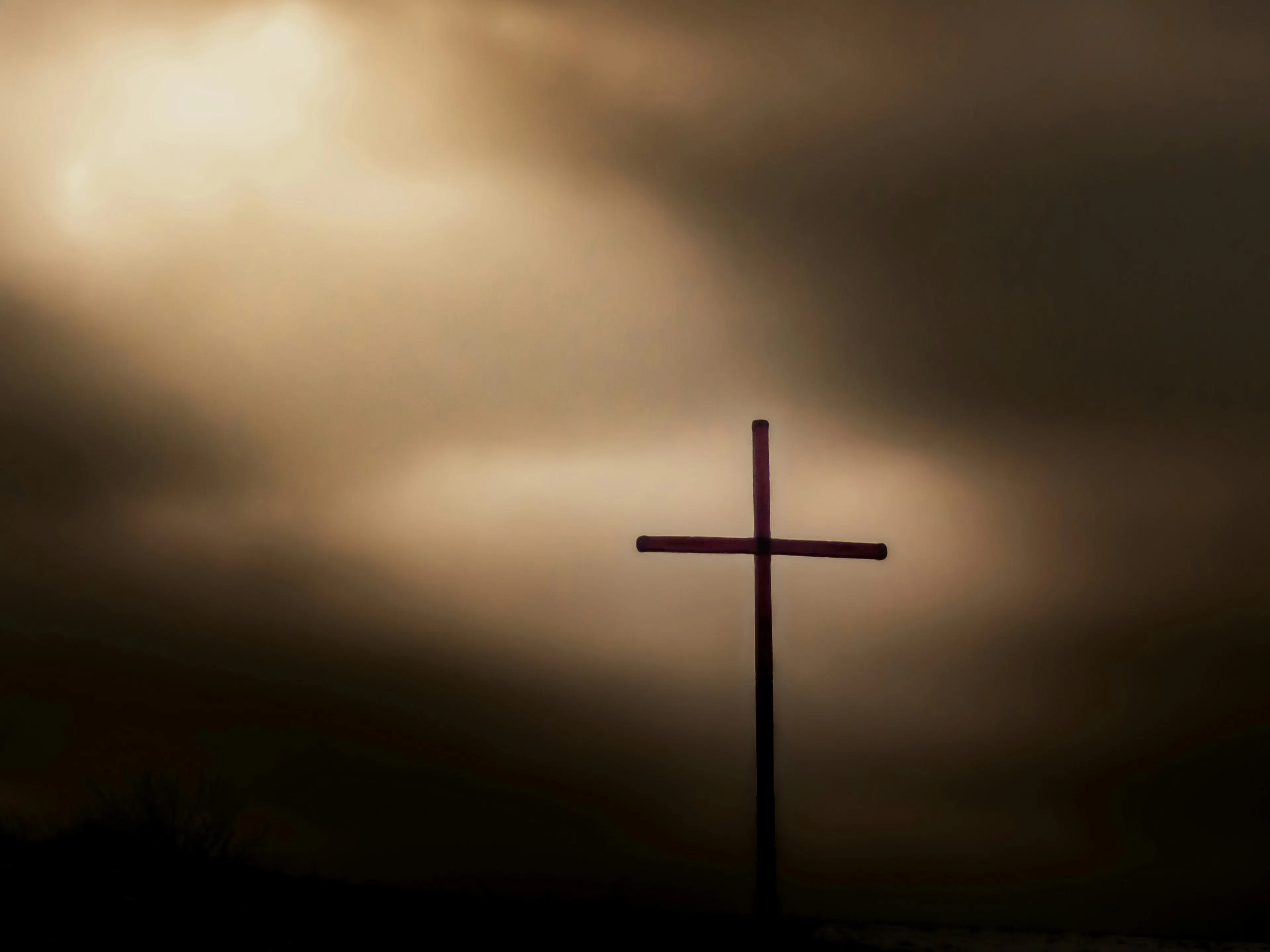 Silhouette of a cross against a cloudy sky with light breaking through