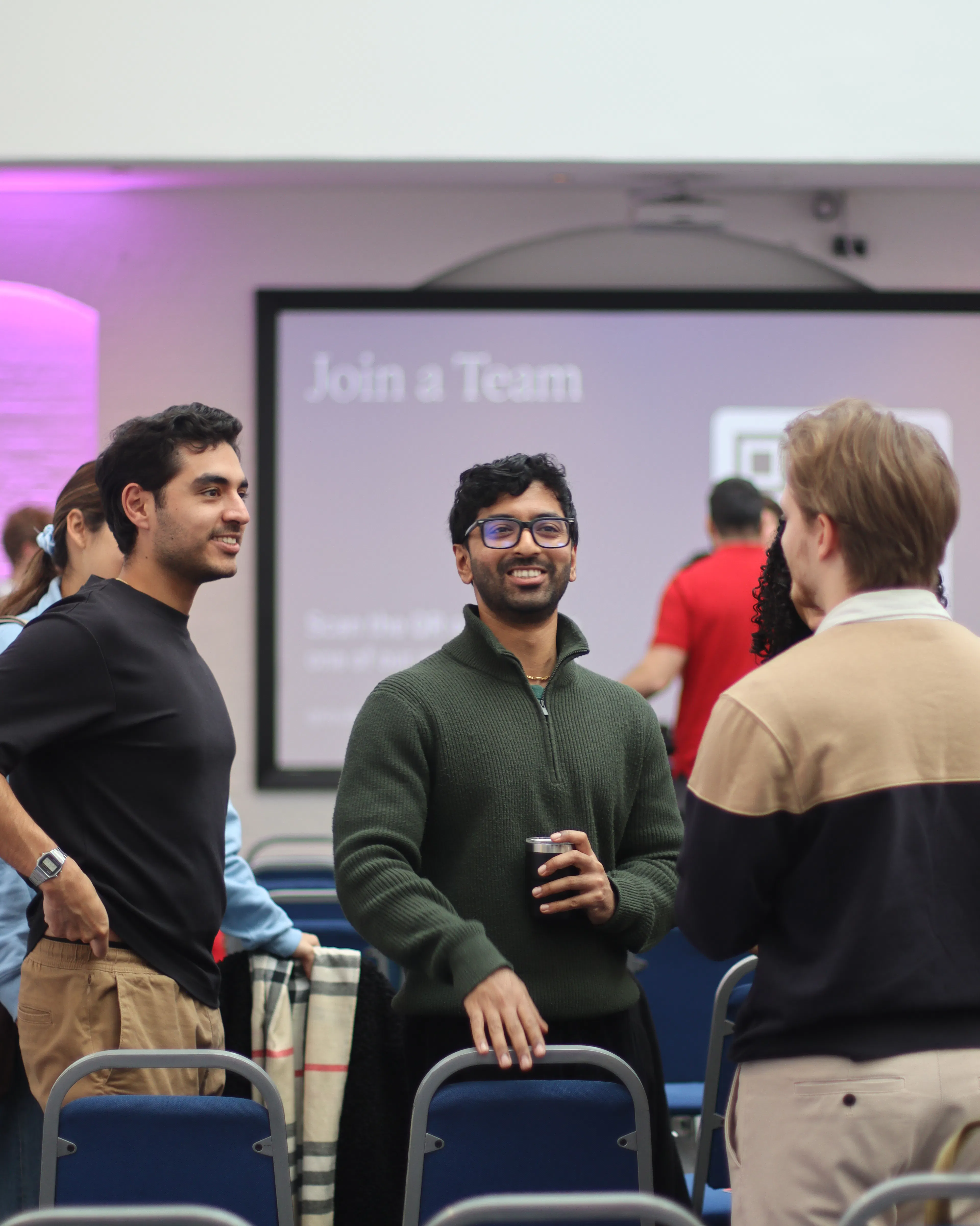 Young men chatting and smiling among rows of chairs at a church gathering