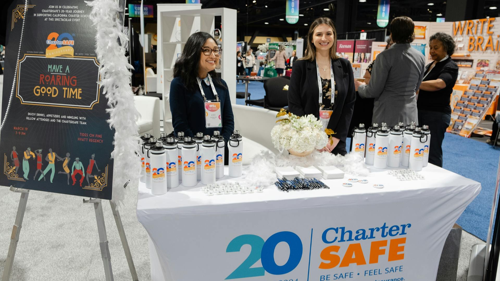 Photo of Charter SAFE representing at conference. Two people standing and smiling behind a table with give-way items.