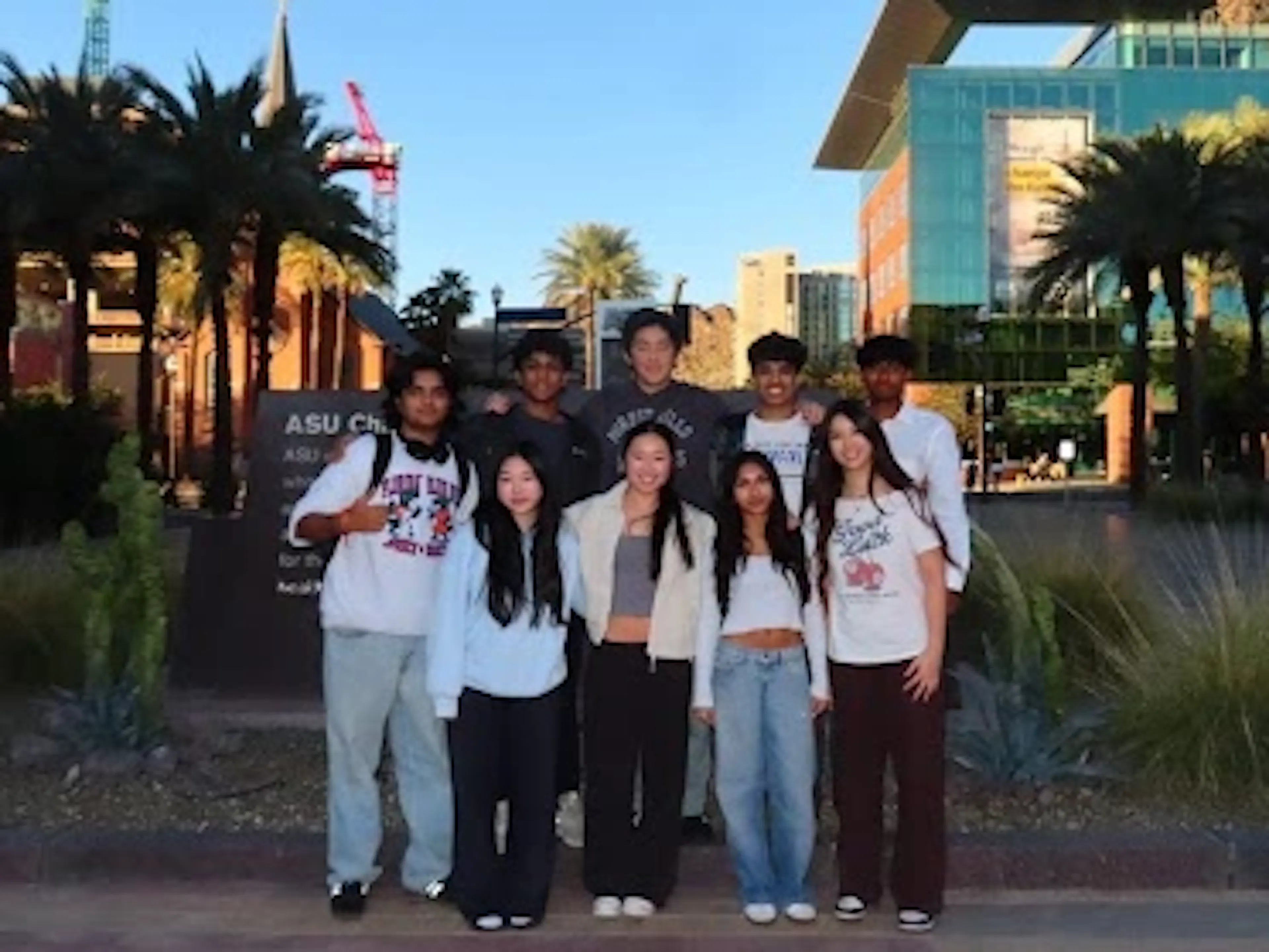 A group of 9 students pose for a photo outside in front a college