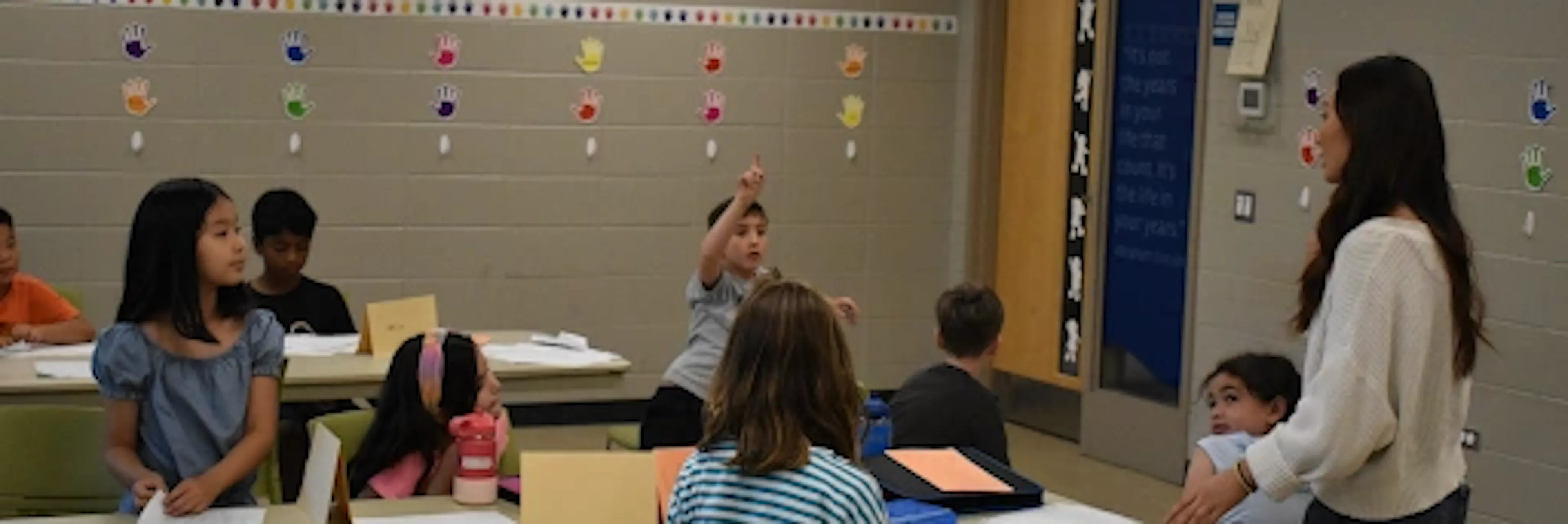 In a classroom, one student raises their hand while other students watch