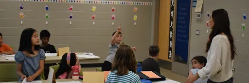 In a classroom, one student raises their hand while other students watch
