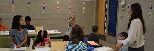 In a classroom, one student raises their hand while other students watch