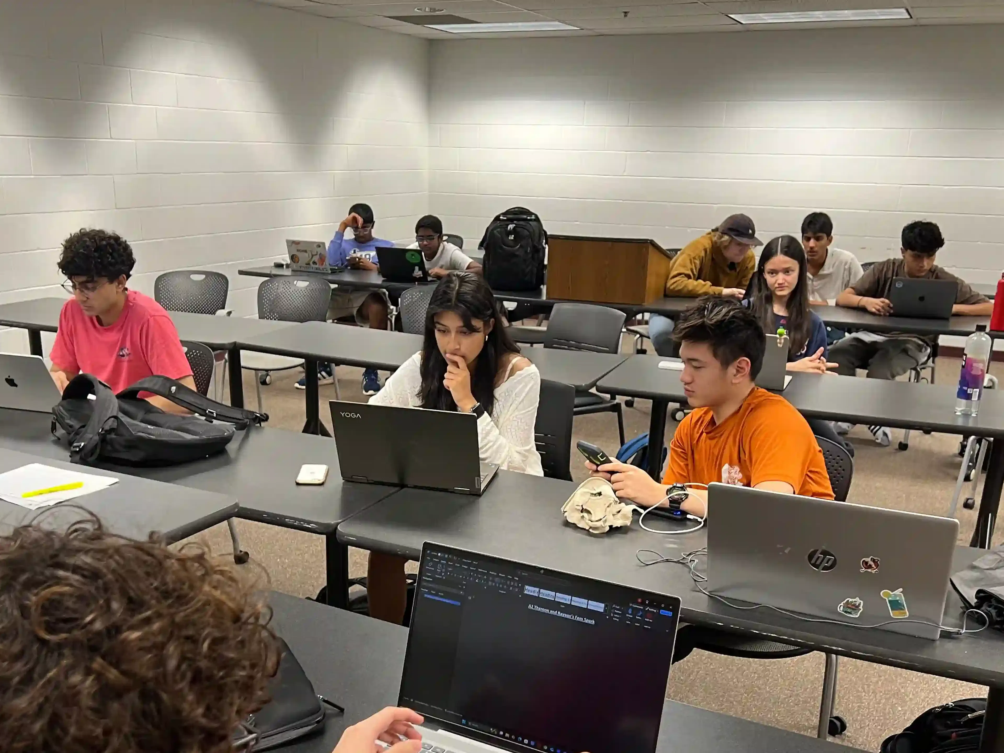 Students sitting at tables working on laptops discuss something