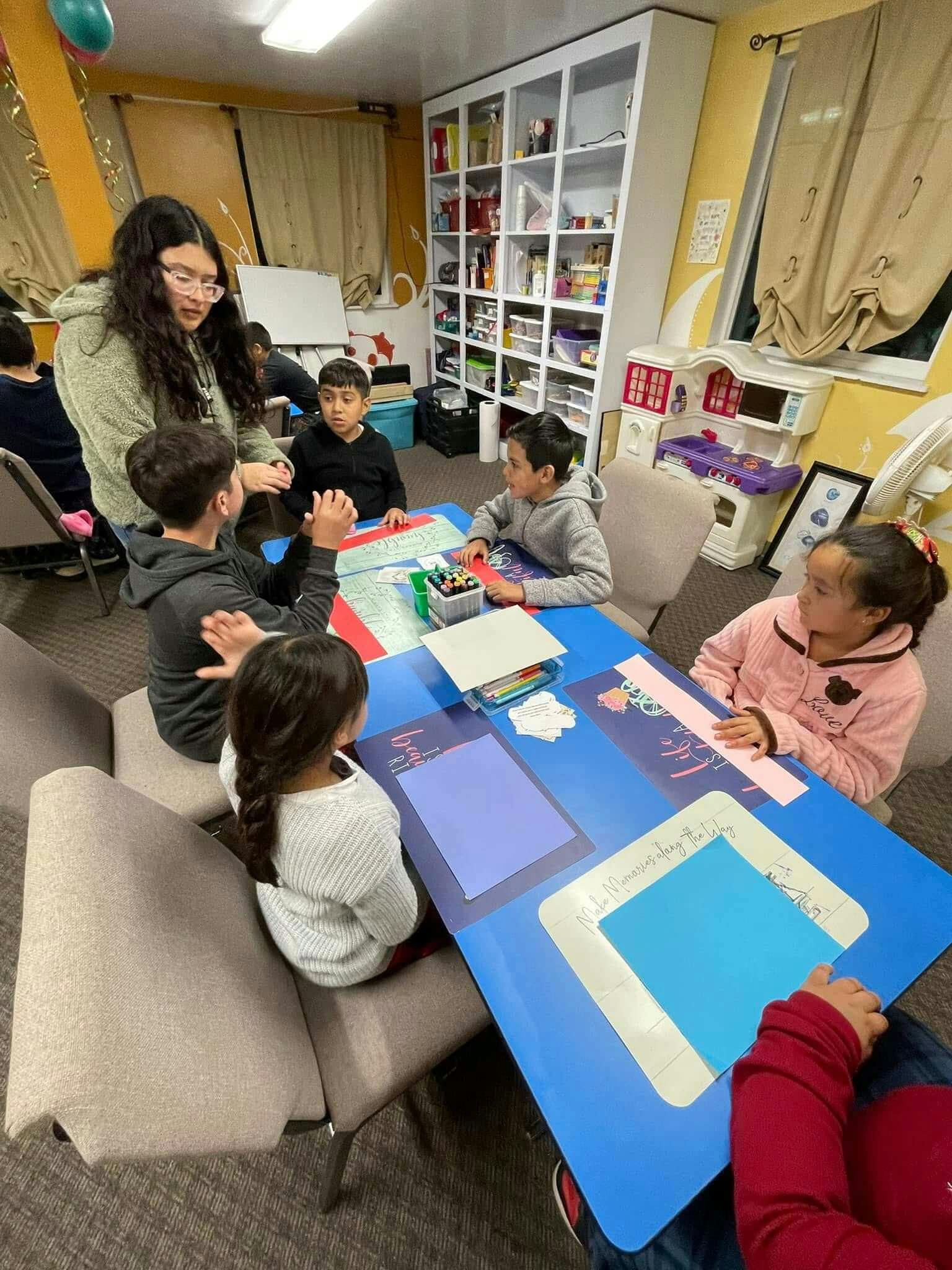 Niños sentados en una mesa, concentrados en colorear dibujos relacionados con una historia bíblica.