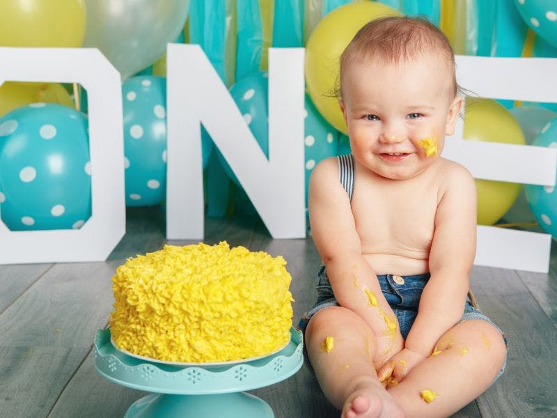  a baby boy next to a yellow cake celebrating his first birthday