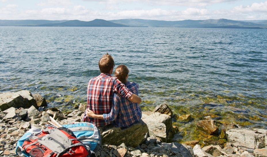 a couple sitting on rocks close to water overseeing mountains