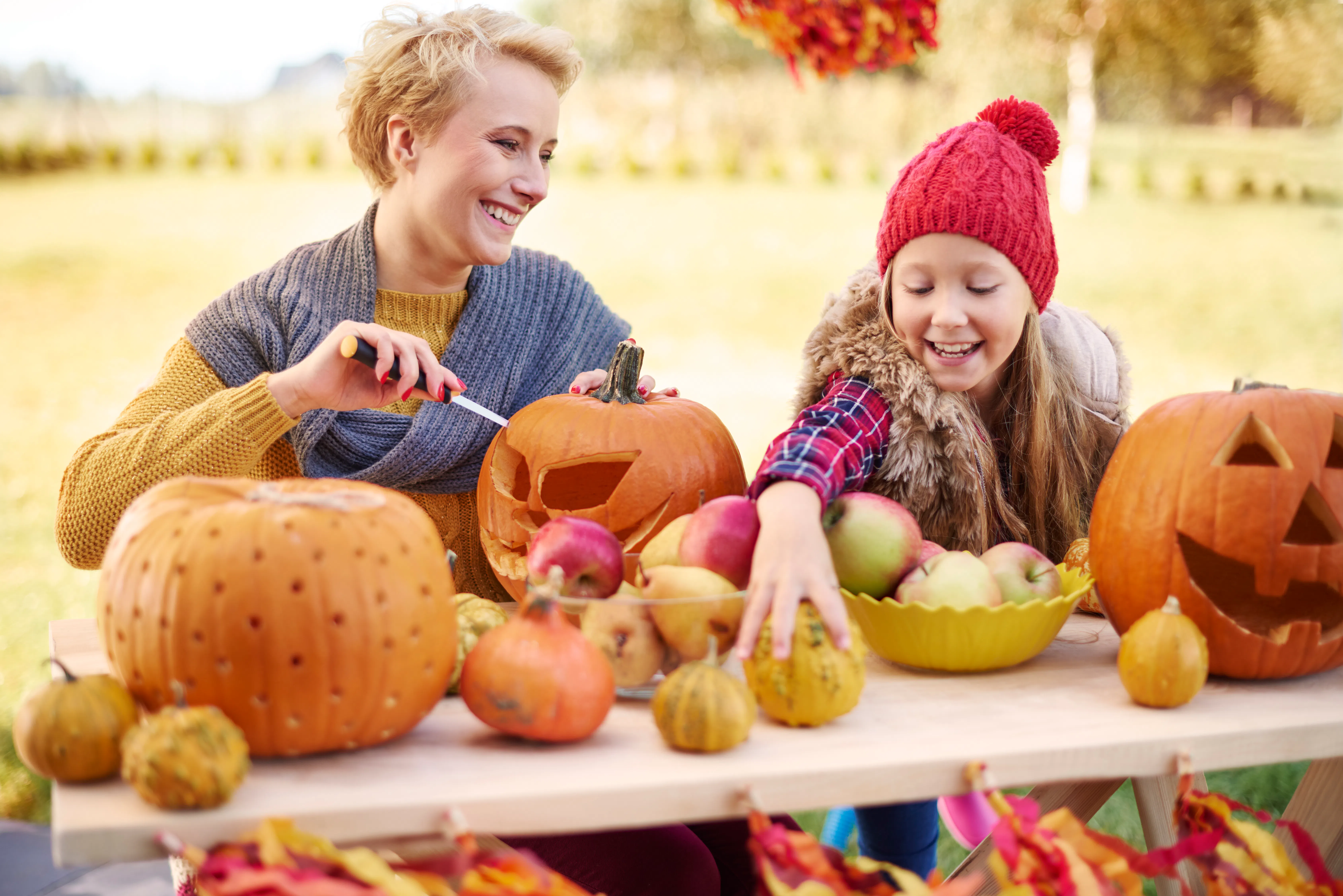 Mother and daughter carving pumpkins outdoors.