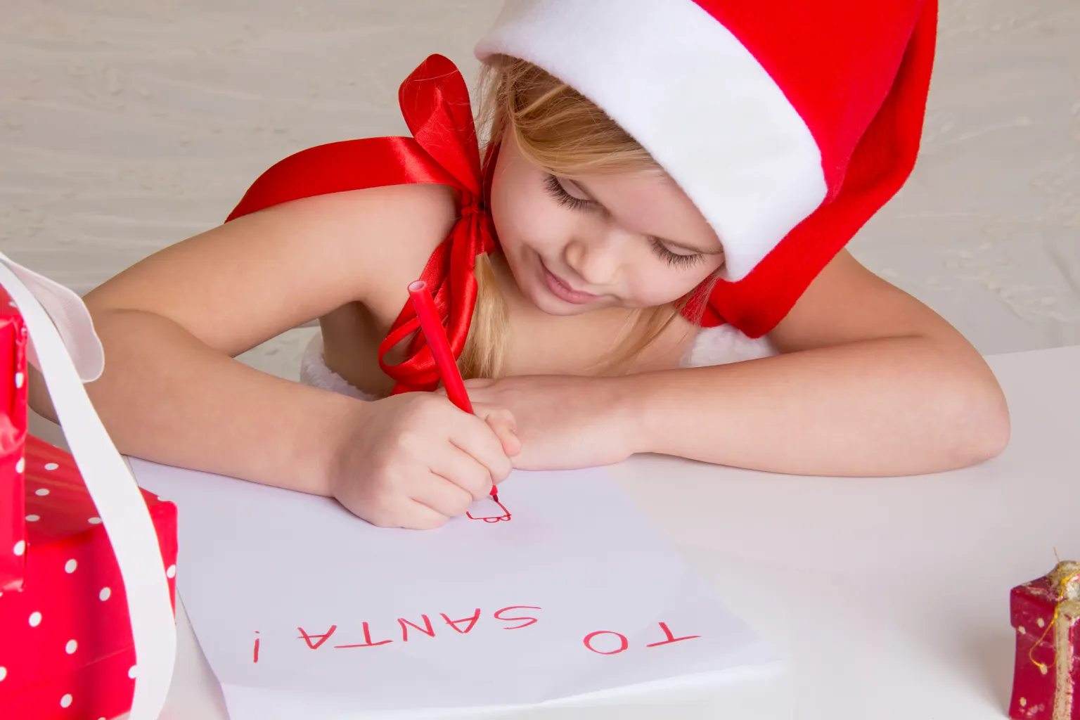 Little girl writing a Letter to Santa with a red crayon.