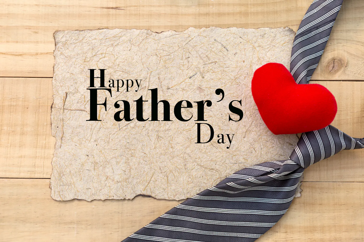 Happy Father’s Day text on a rustic paper background with a tie and red heart symbolizing love for dads