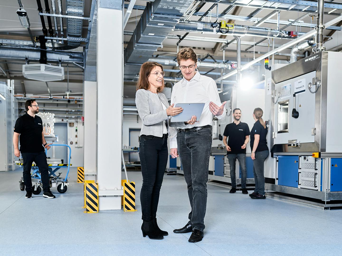 Two people standing in a production room talking about a worksheet