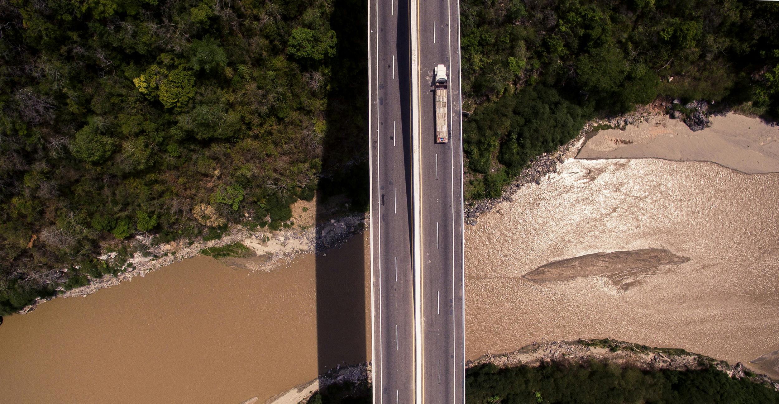 Abbildung zeigt eine Brücke in einer bewaldeten Umgebung von oben, über die ein Lastwagen fährt