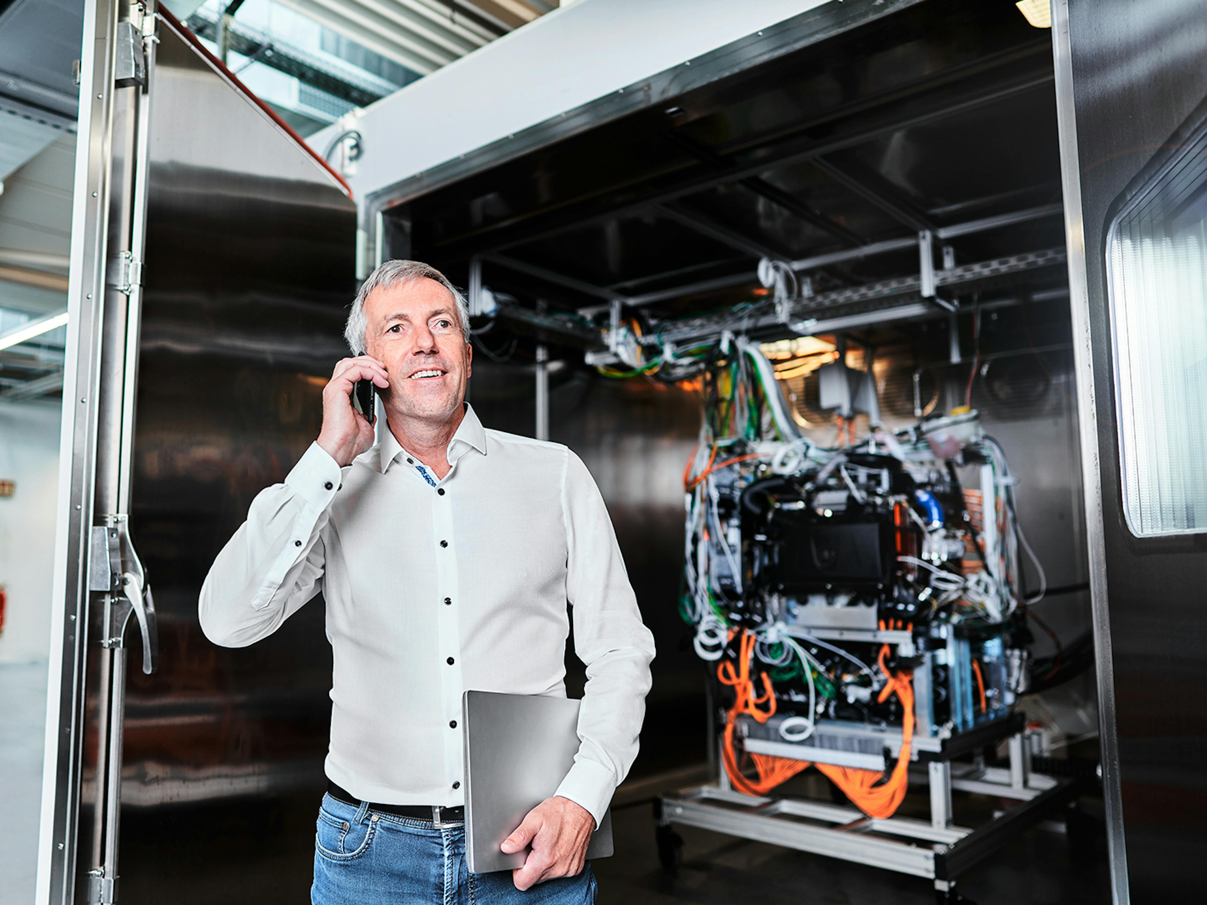 Ein Mann steht mit einem Telefon in der Hand vor einem technischen Gerät und telefoniert