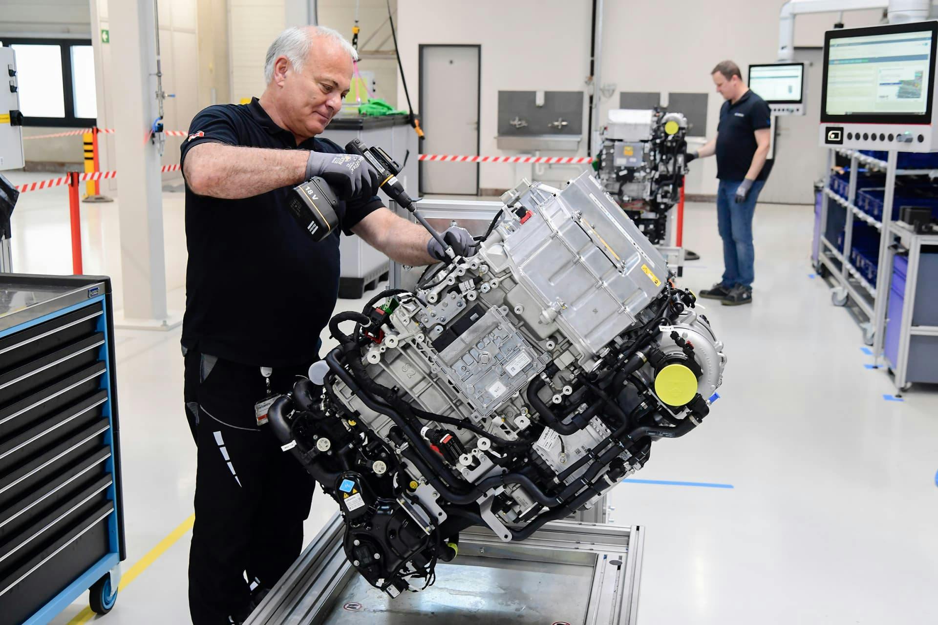 A technician screws a motor unit onto a test station using a cordless screwdriver, with a colleague in the background.