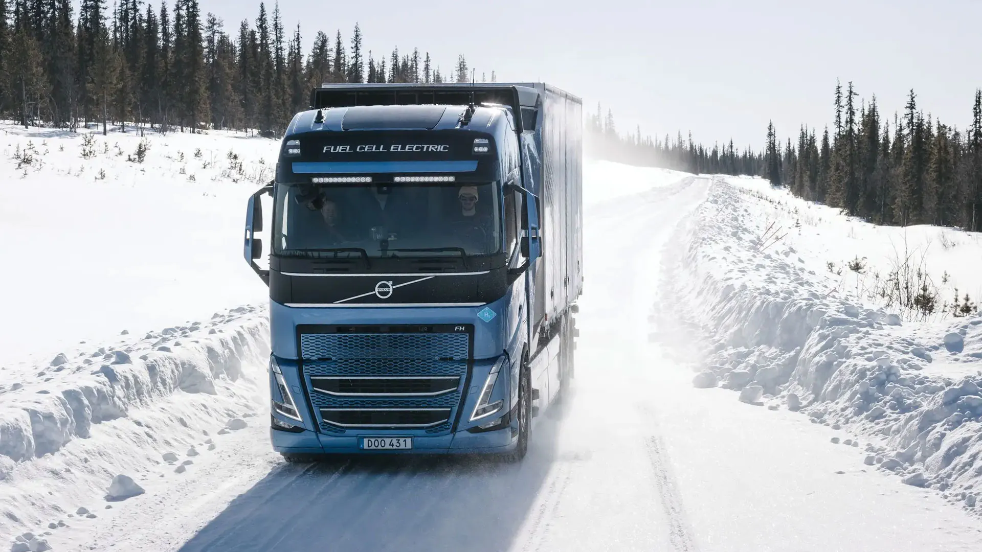 Ein blauer Volvo-Brennstoffzellen-Elektro-Lkw fährt auf einer schneebedeckten Straße, die von Schneewehen und Bäumen gesäumt ist, in einer Winterlandschaft.