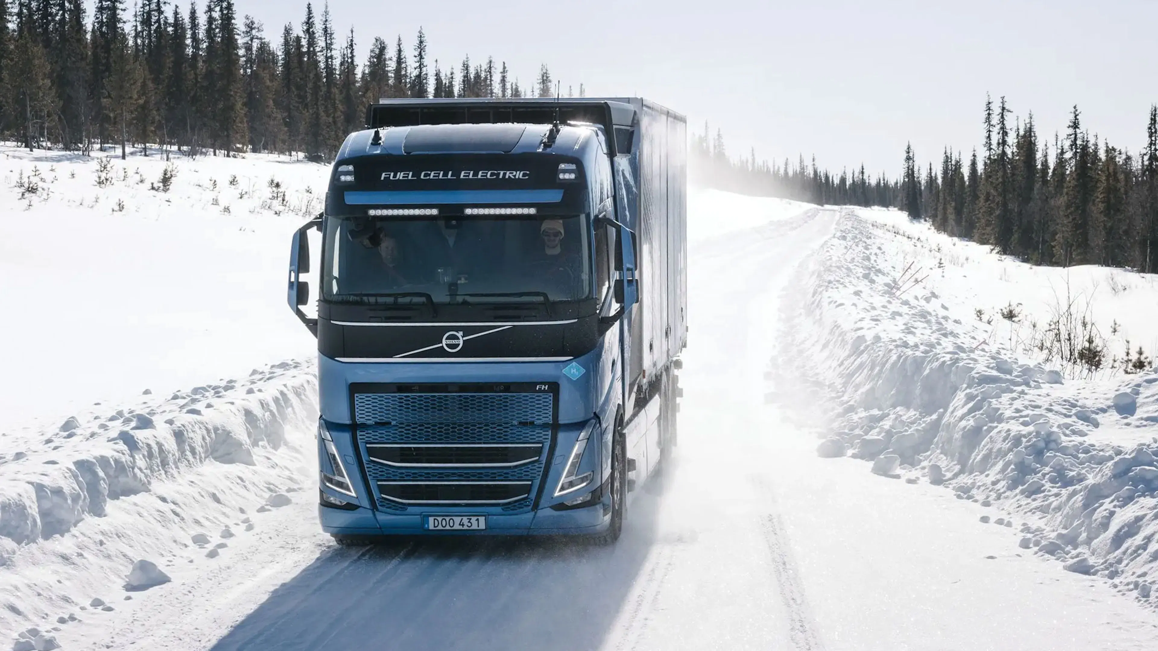 Ein blauer Volvo-Brennstoffzellen-Elektro-Lkw fährt auf einer schneebedeckten Straße, die von Schneewehen und Bäumen gesäumt ist, in einer Winterlandschaft.