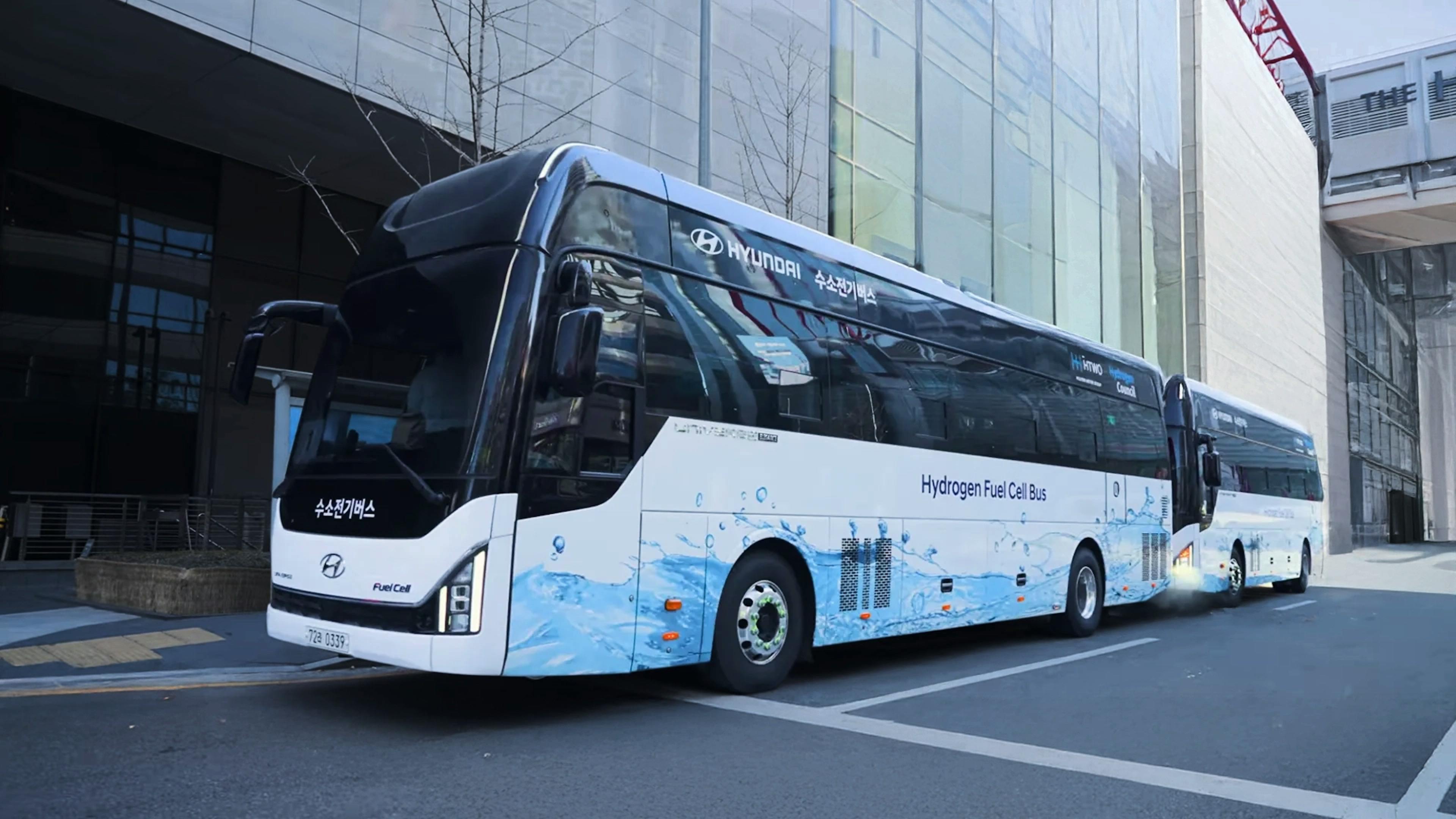 Zwei Wasserstoffbusse von Hyundai fahren in einer modernen, urbanen Umgebung
