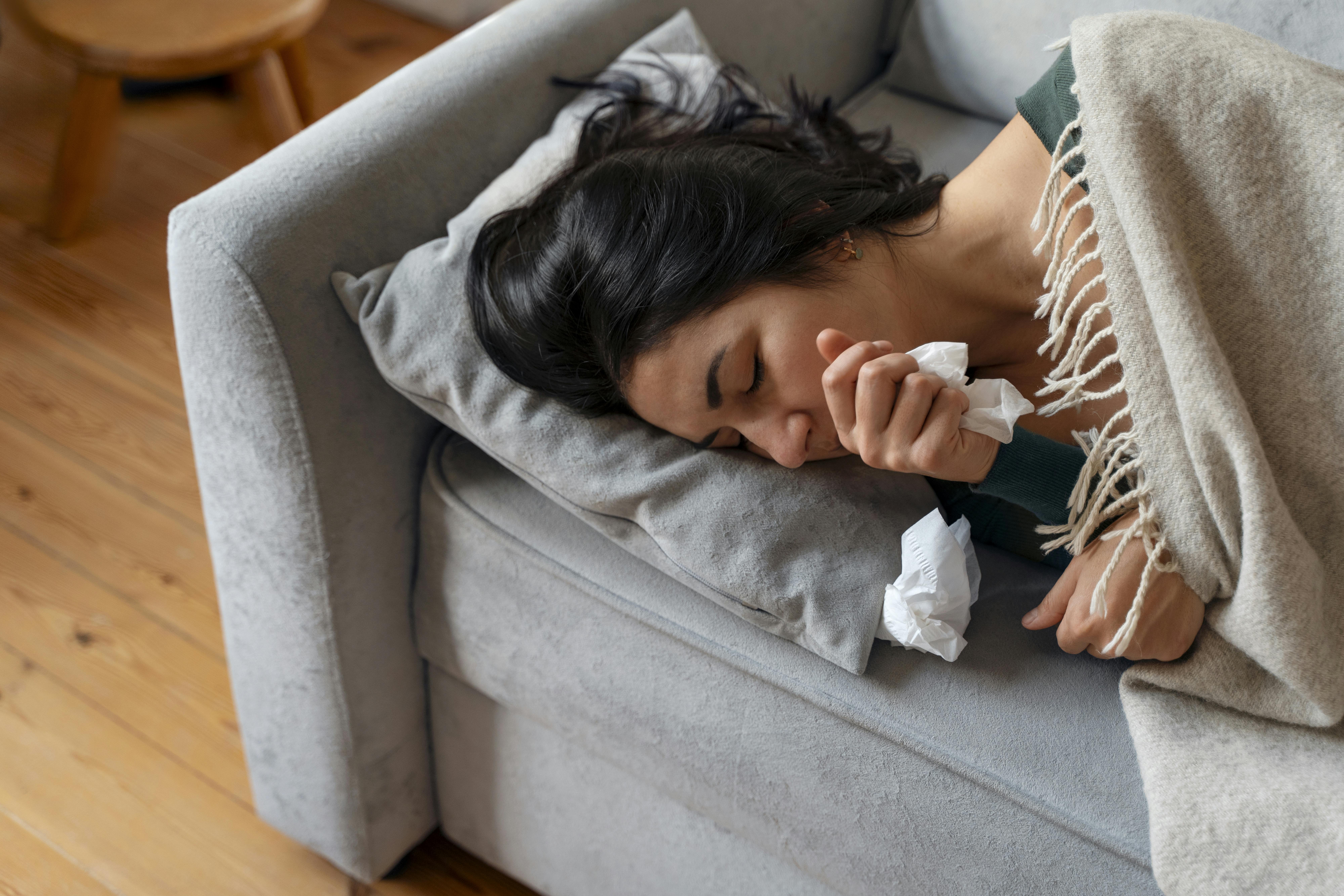 Woman is sick and asleep on a couch with tissues in hand