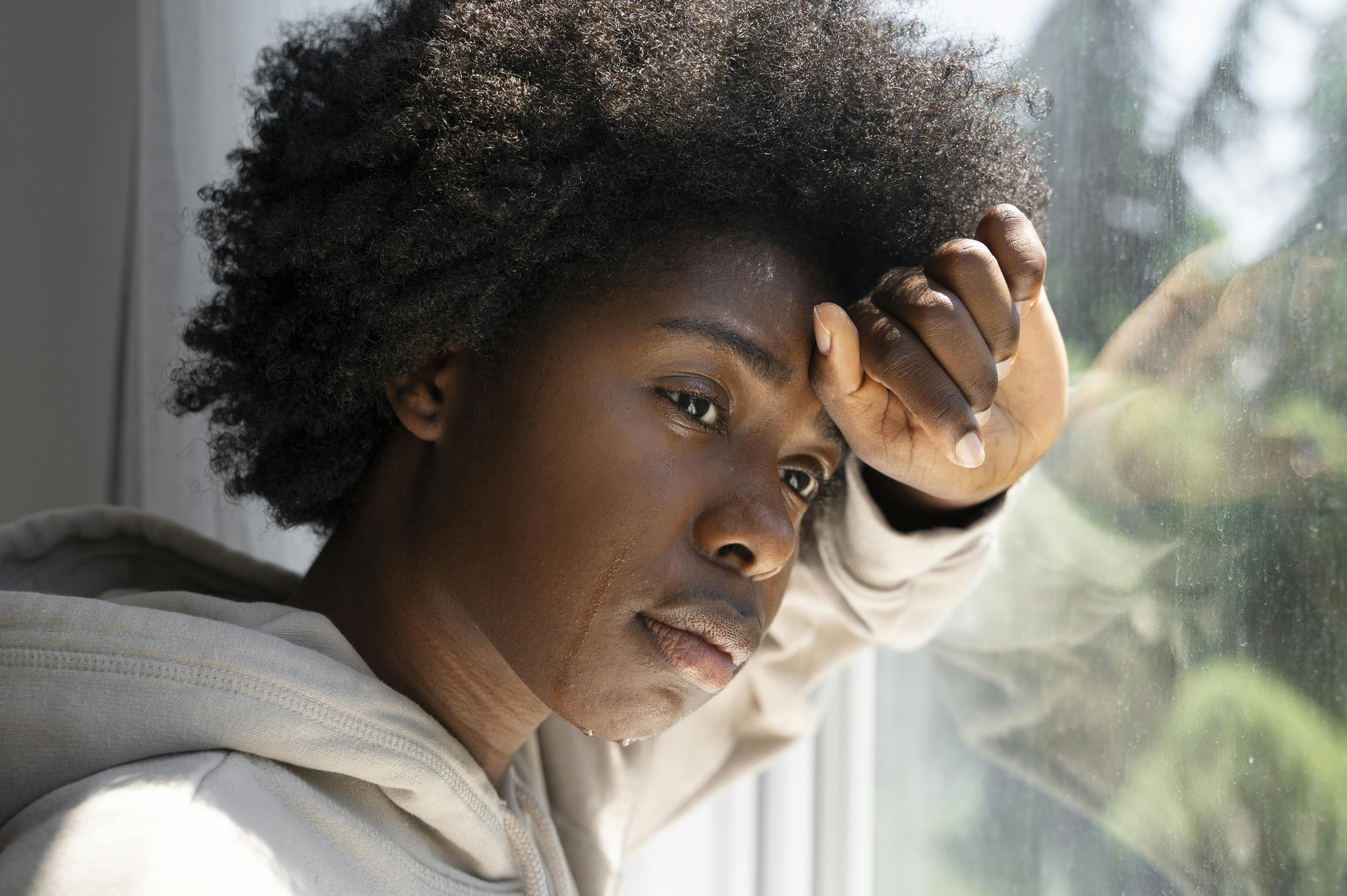 Black female looking depressed while tears stream down cheek as she stares out window