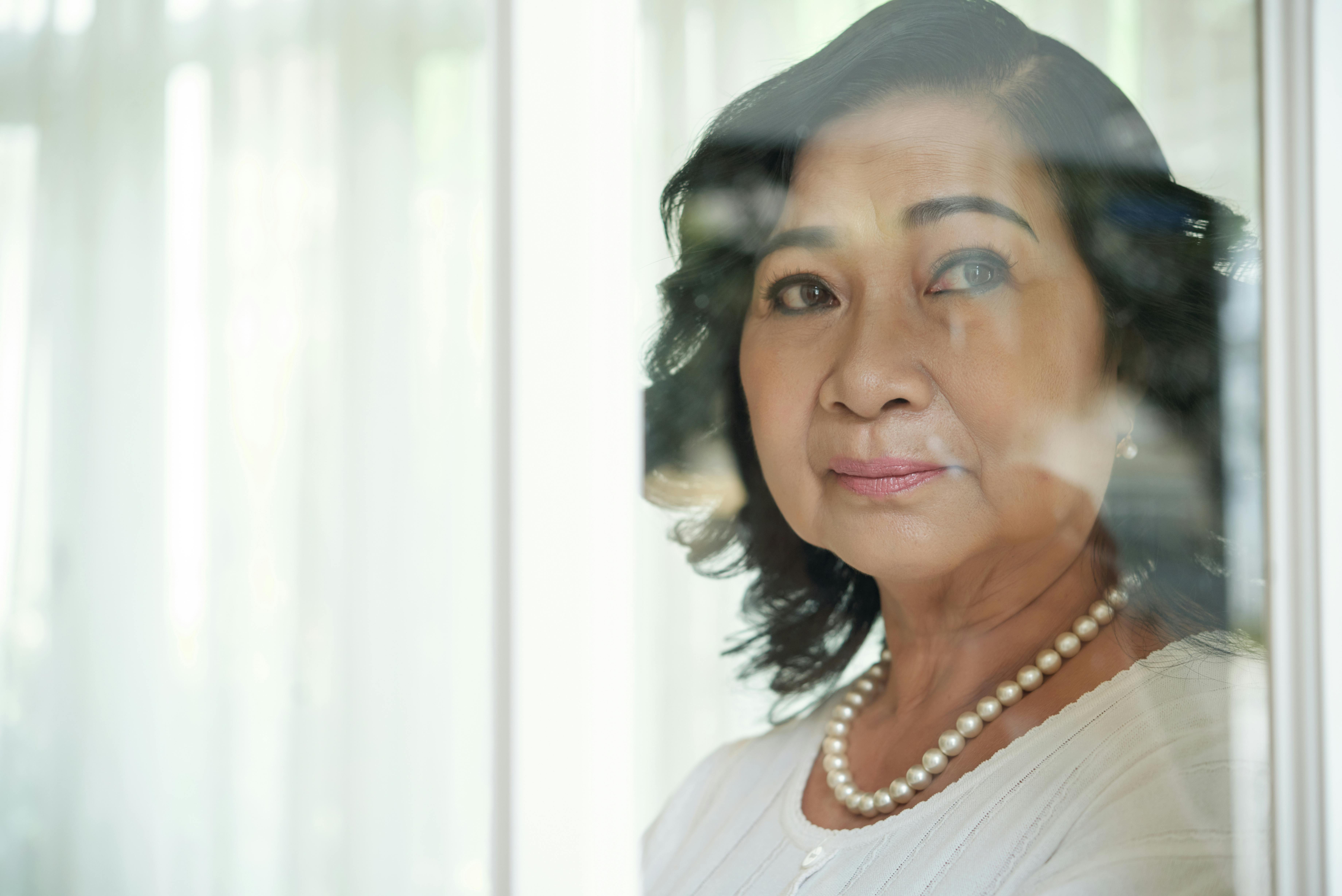 Older Asian woman looks pensively out of a window