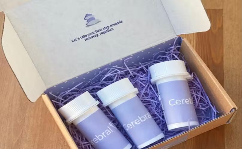 Three Cerebral prescription bottles are in a box with lavender crinkle cut packaging paper