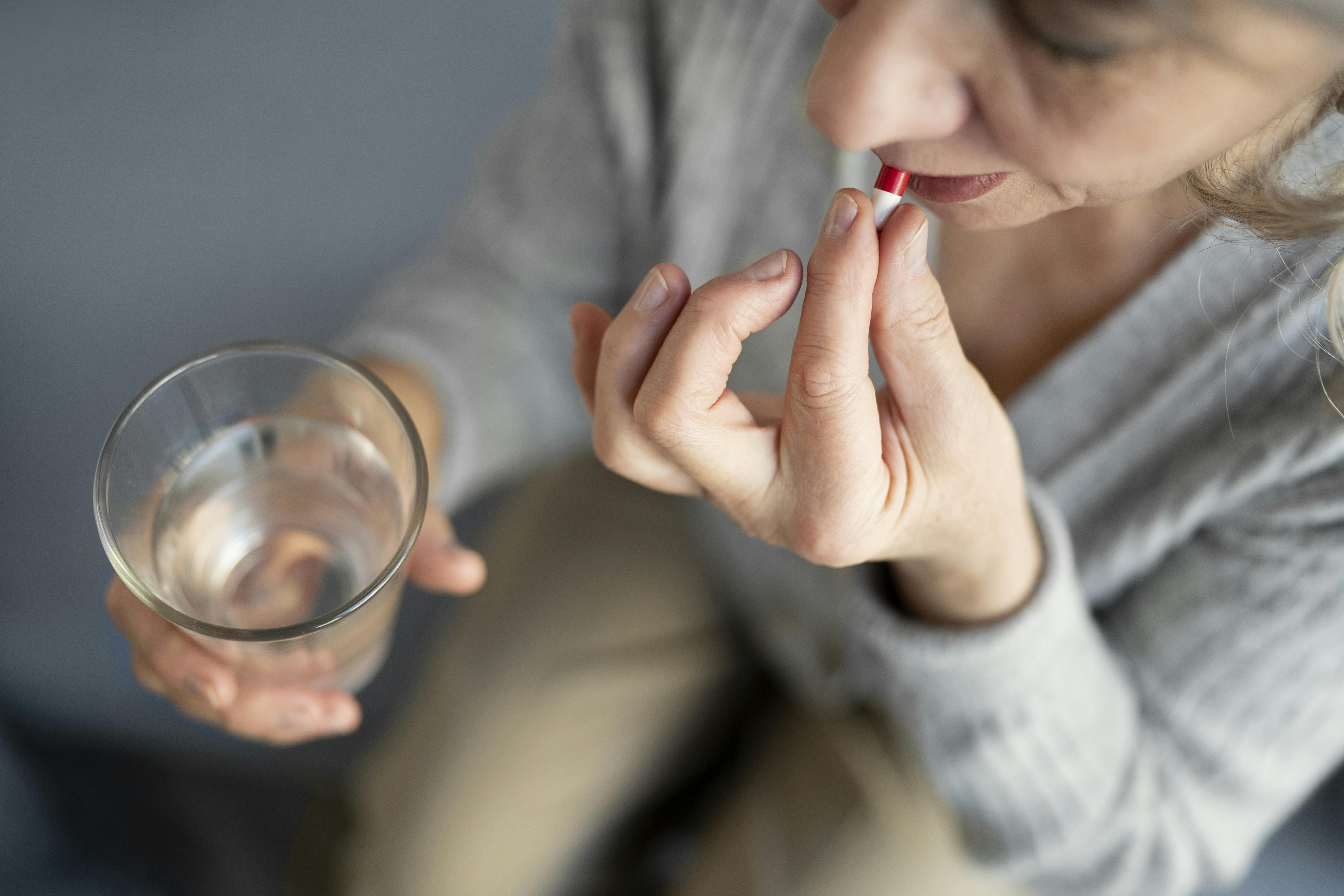 Older white woman takes medication with a glass of water