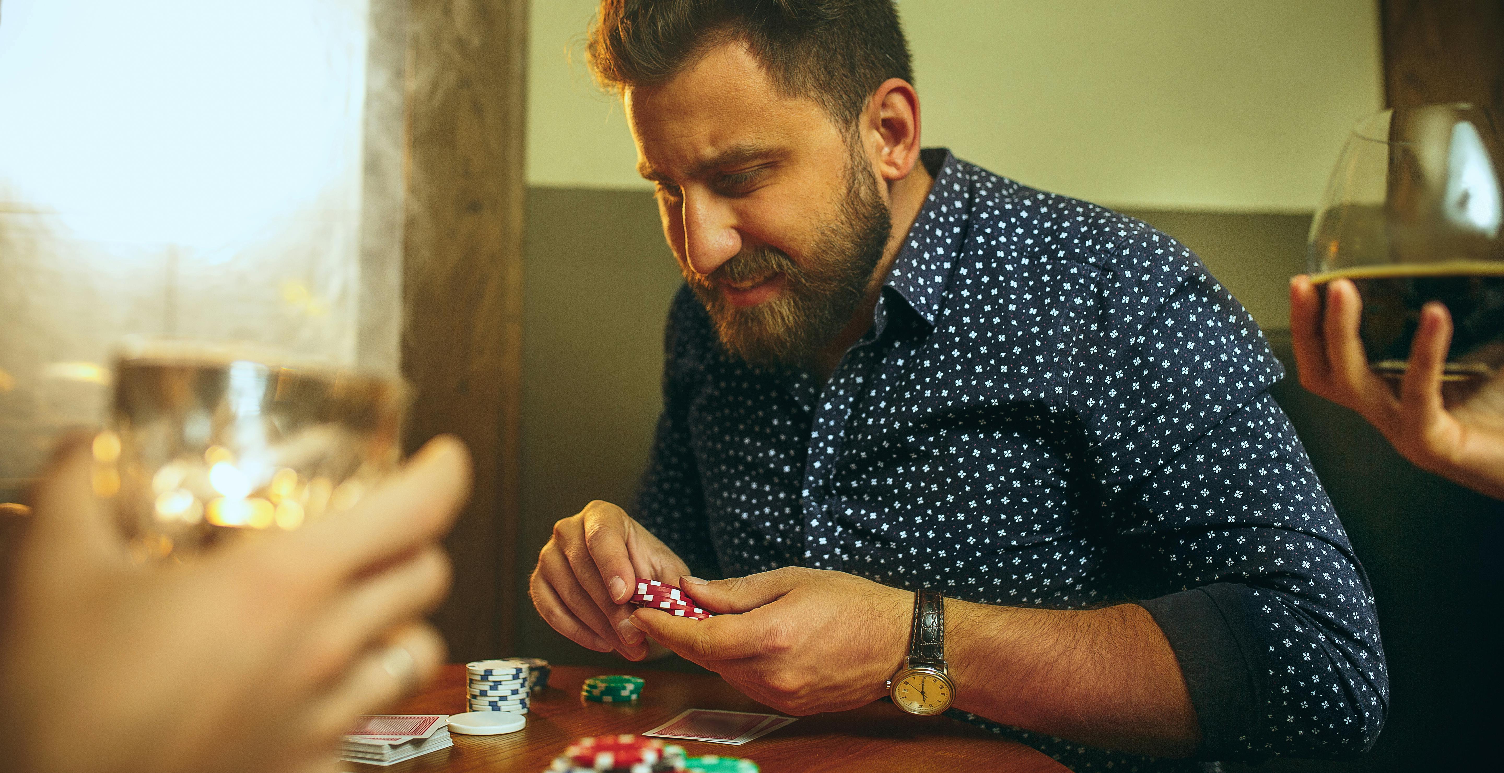 Man in blue and white shirt sits at table playing poker