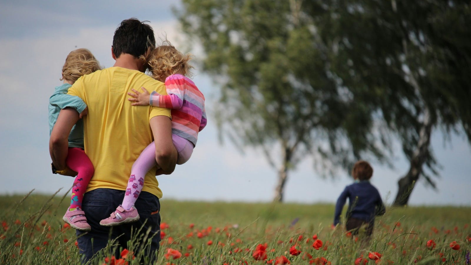 Papà tiene in braccio i suoi figli in un campo di papaveri