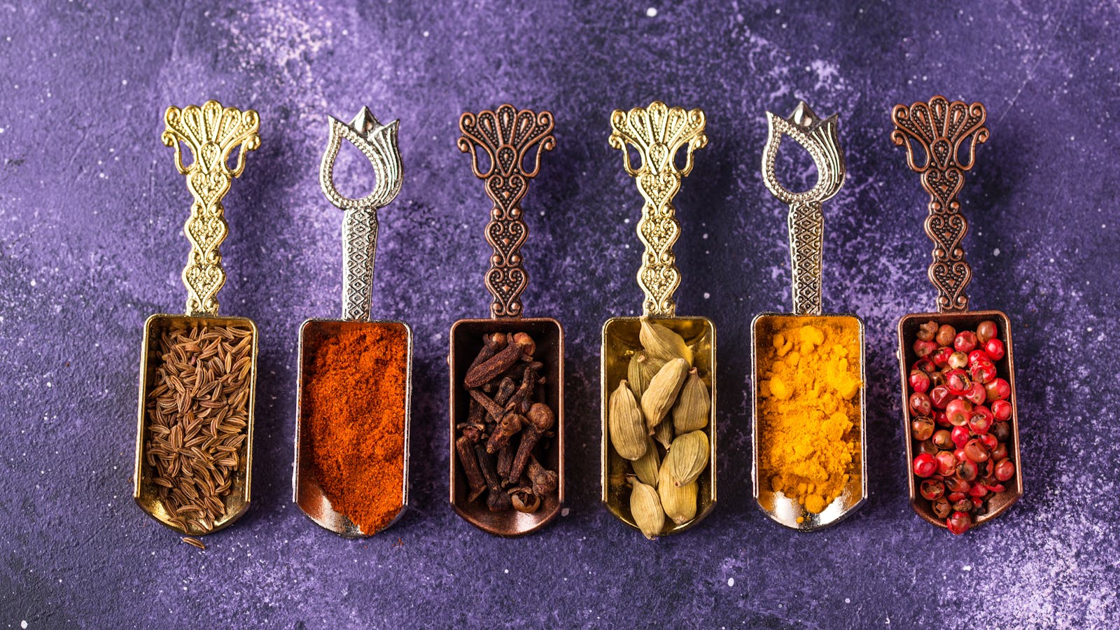 Various types of spices on metal spoons