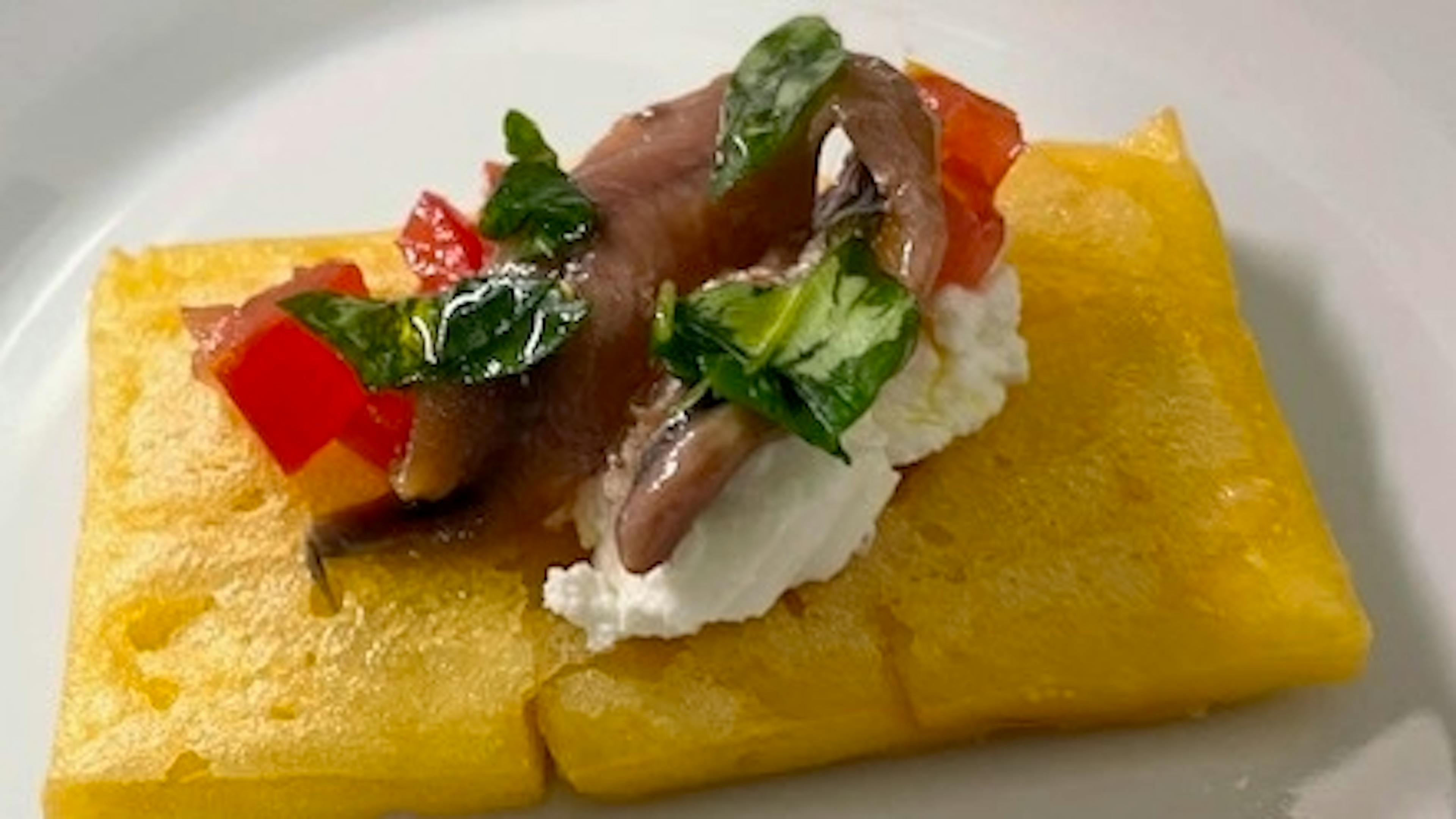 Chickpea polenta with anchovy fillets, ricotta, tomatoes and basil leaves
