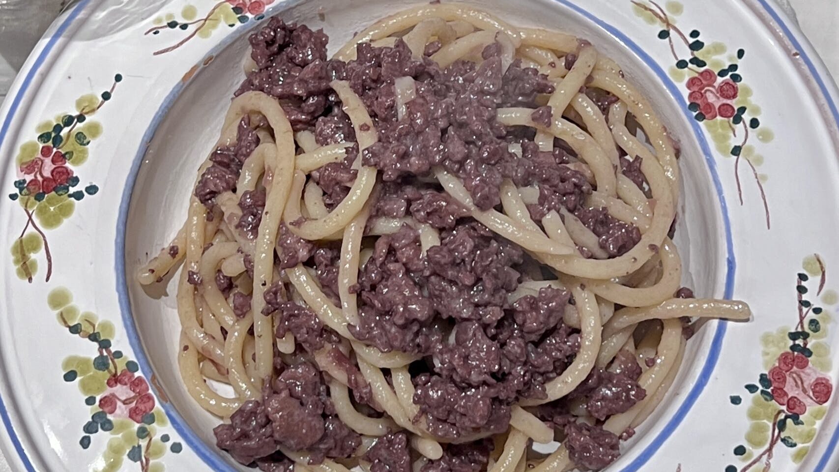 Plate of handmade pici pasta with Certaldo onions, Tuscan sausage, and Chianti red wine sauce