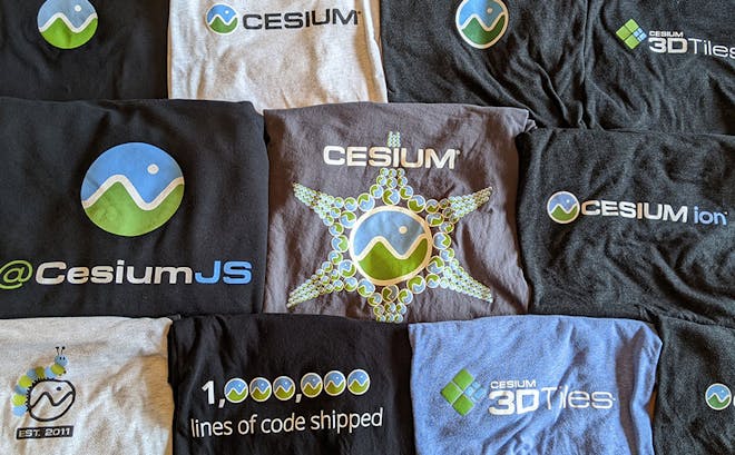 Eleven t-shirts in different colors folded so you can see the Cesium logo and design on each of them.