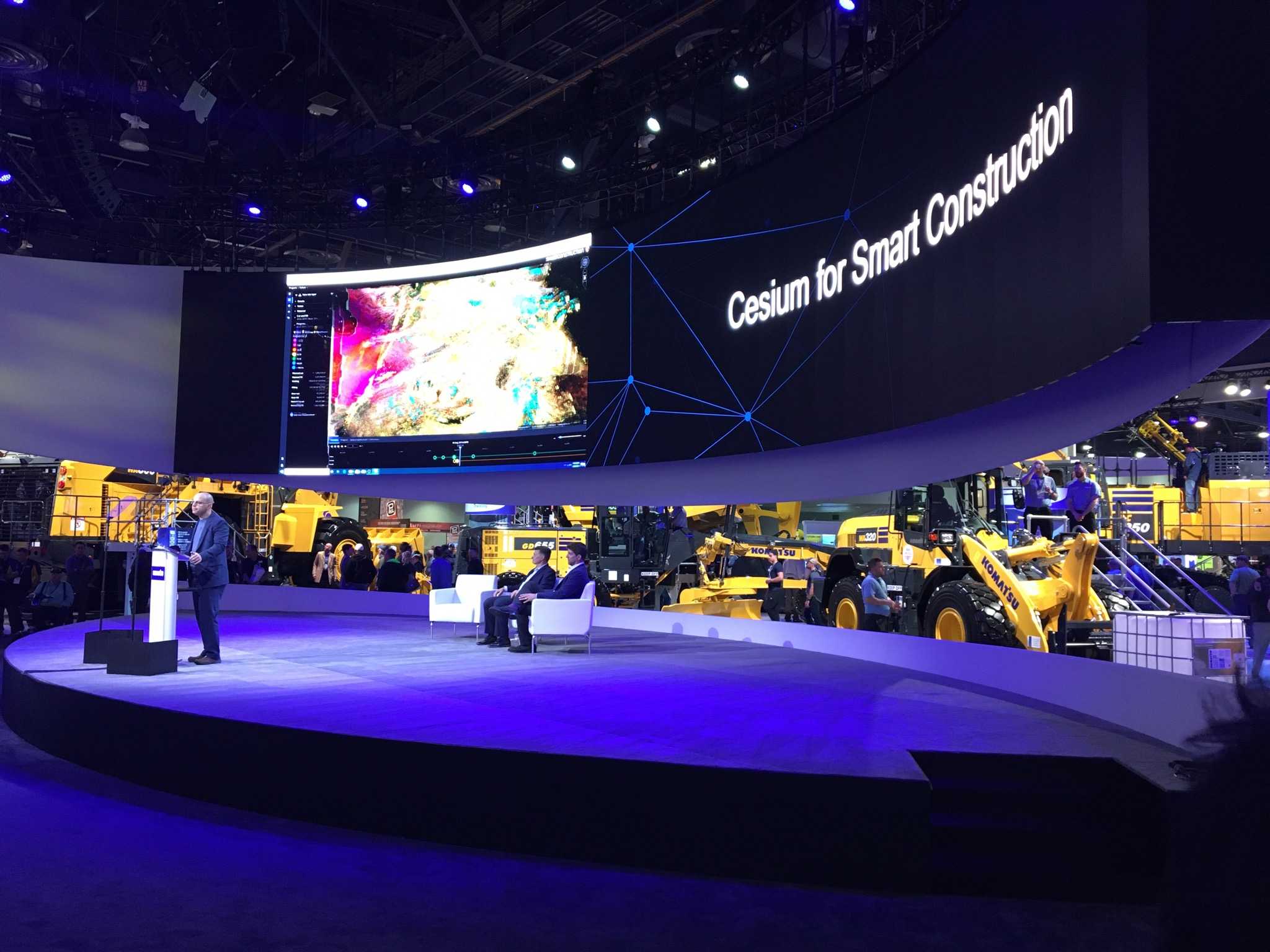 Cesium CEO Patrick Cozzi stands at a podium in front of a wide screen that says "Cesium for Smart Construction" at ConExpo 2020 in Las Vegas