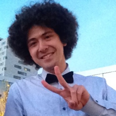 A man with long curly hair wearing a bow tie smiles.