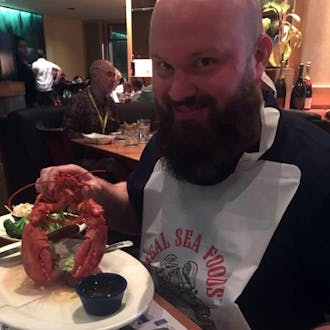 Tom Fili holding a cooked lobster above a plate.