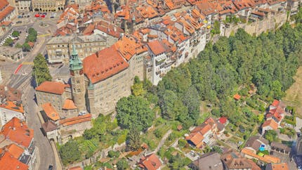 Old City of Fribourg, Switzerland, in ultra high-def 3D model by Uzufly. Orange-red roofs, stone buildings, green bell tower, green trees, yellow markings on roads.
