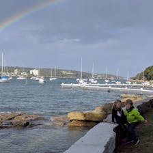 Two young children with a rainbow over a harbor. 