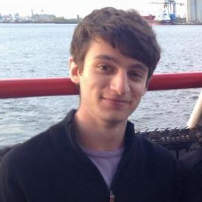 A man smiles while standing in front of a body of water.
