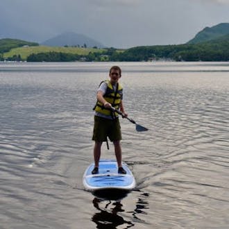 Ian Lilley paddleboarding on a lake with hills in the background.