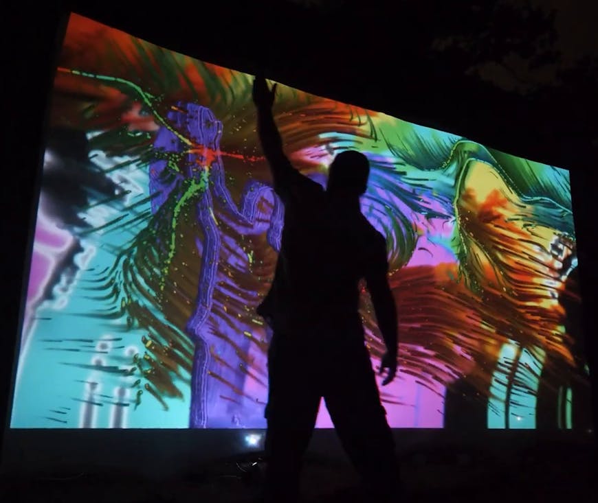 Cory Barr is silhouetted by colorful art resembling feathers or palms.