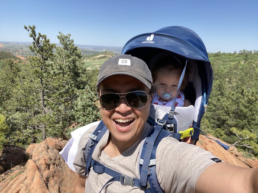 Brian Langevin hikes in Colorado Springs, Colorado, with his daughter. They are surrounded by pine trees and red rocks.