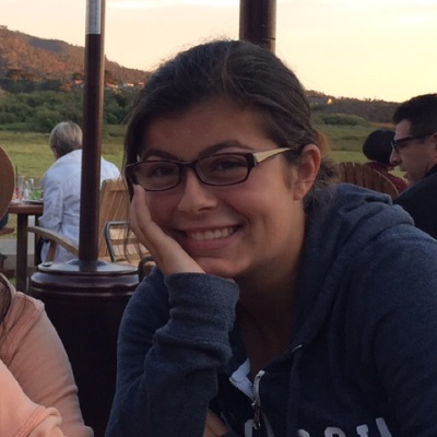 A woman in glasses rests her chin on her hand and smiles.
