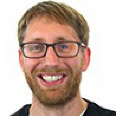 A man with glasses and a beard smiles.