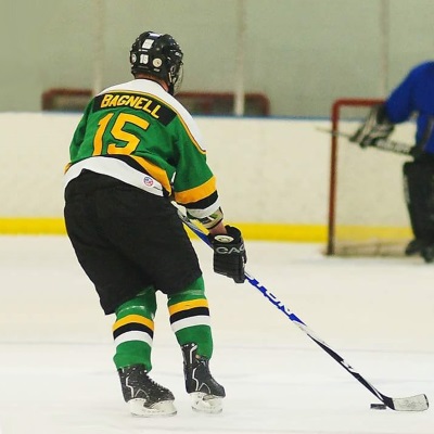 A man skates on ice wearing in a green and gold hockey uniform.