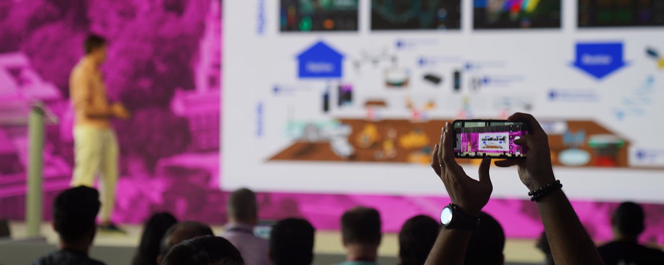 An attendee of the 2025 Cesium Developer Conference in Philadelphia takes a photo with their phone of a presenter session.